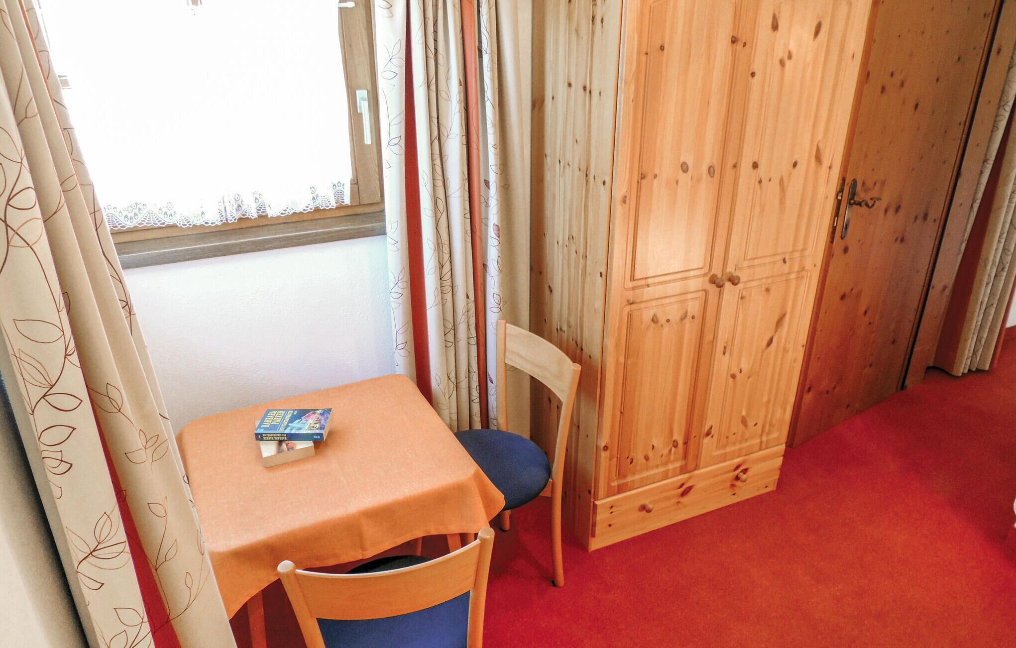 A small room with a wooden cabinet, a table with a chair, and a window with curtains.