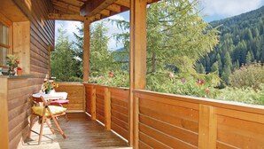 A wooden deck with a table and chairs, overlooking a forested mountain area. - wunderschoene Ferienwohnung (Obernberg)