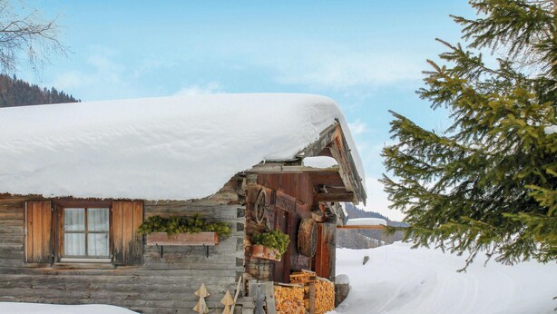 A rustic log cabin with a snow-covered roof, wooden shutters, and a stone foundation. - wunderschoene Ferienwohnung (Obernberg)