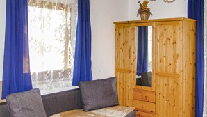 Een kamer met een houten garderobe, een grijze bank met kussens en een raam met blauwe gordijnen.
