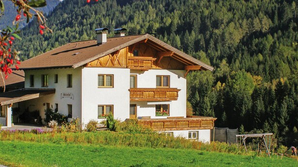 Een huis met twee verdiepingen, een schuin dak, een houten balkon en een tuin aan de voorkant.
