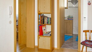 Een hal met een houten boekenkast vol boeken en een rode Novasol doos. Op de vloer ligt een blauw tapijt en een stoel is zichtbaar.
