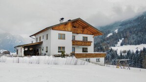 Een chalet met twee verdiepingen en een houten balkon, omringd door met sneeuw bedekte bergen.