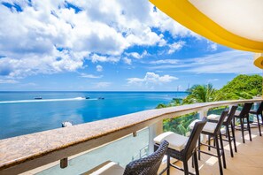 A balcony with a view of the ocean and boats, wicker chairs, and a yellow awning.