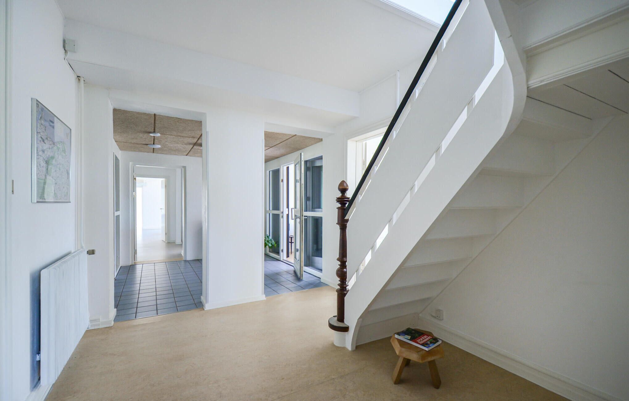 A spacious hallway with a wooden staircase leading to upper floors, a radiator, and a small table with a book.