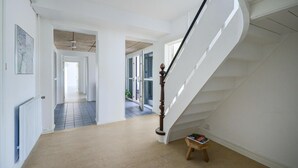 En rymlig hall med en trappa i trä som leder upp till de övre våningarna, ett element och ett litet bord med en bok på.