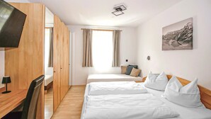Ein Hotelzimmer mit zwei Betten, einem Schreibtisch, einem Fernseher und einem Fenster mit Vorhängen.