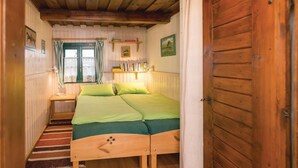 Een gezellige kamer met een houten bed, een klein nachtkastje, een raam met kantgordijnen en een deur.