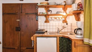 Een compacte keuken met houten kastjes, een Bosch koelkast, een koffiezetapparaat en een plank met servies en bestek.