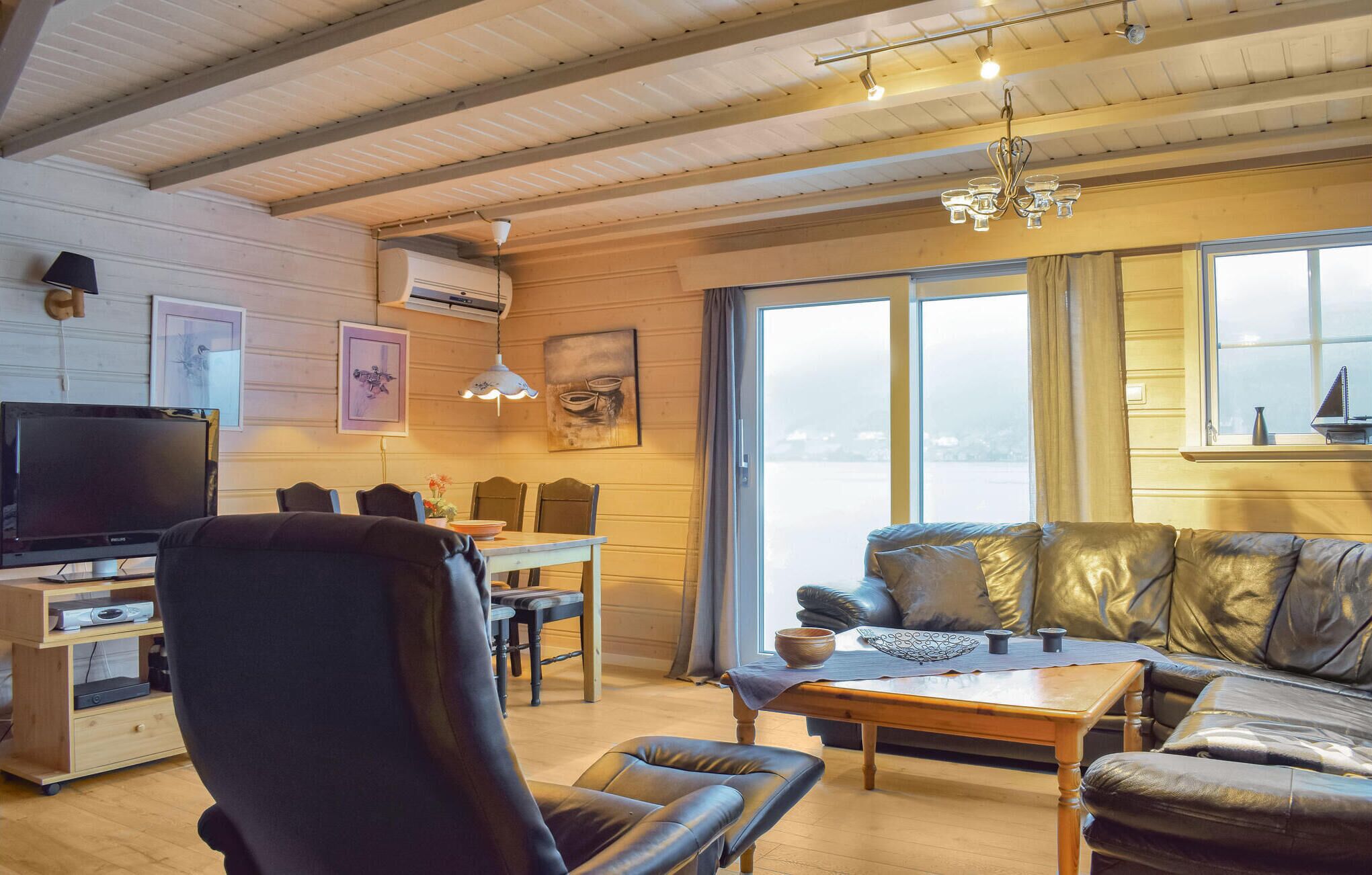 A cozy living room with a wooden ceiling, a television, a dining area with chairs and a table, and a sofa with cushions.
