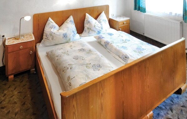 Una cama de madera con ropa de cama floral, una mesita de noche con lámpara y un aparador con toma de corriente.