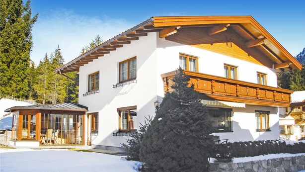 Ein zweistöckiges Chalet mit Holzbalkon, großen Fenstern und verschneitem Gelände.