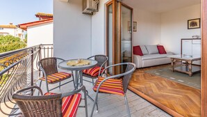 Un balcon avec des fauteuils et une table en osier, un canapé avec des coussins et un plancher en bois.