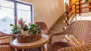 Un coin de pièce avec des meubles en osier, une petite table et une fenêtre ornée de plantes.