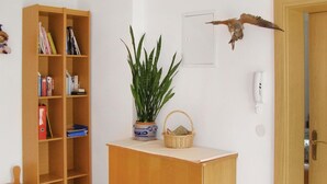 Een kamer met een houten boekenplank, een potplant, een rieten mand, een bevestigde vogel en een witte telefoon aan de muur.