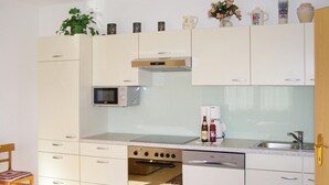 Een praktische keuken met een magnetron, oven en vaatwasser. Er is een spoelbak met kraan, een stoel en een kleine tafel.