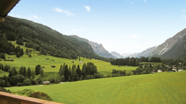 Een bergachtig landschap met groene velden en verspreide gebouwen.