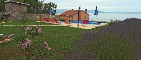 Un área de piscina con sillones reclinables, un edificio de piedra y vistas al agua.