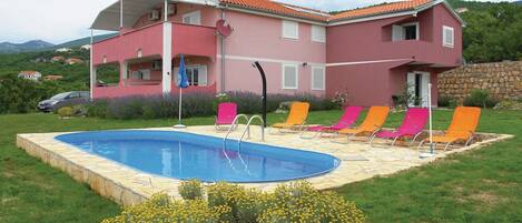 A pink villa with a swimming pool, surrounded by colorful lounge chairs and a stone wall.