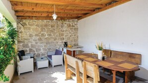 Zona d'estar exterior acollidora amb paret de pedra, sostre de fusta i taula de dinar acompanyada de cadires.