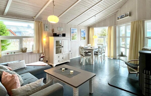 A spacious living area with a sofa, dining table, and chairs, a kitchen area with cabinets, and large windows providing natural light.