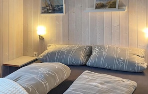A room with two beds, a nightstand, wall-mounted lamps, and framed pictures on the wall.
