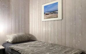 Een eenpersoonsbed met een bedspread met een patroon en kussens, een ingelijst foto van een strandlandschap aan de muur, en houten lambrisering.