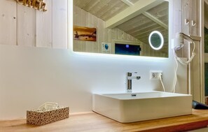 Een badkamer met een witte wastafel, een spiegel met een ringlamp en een zakdoos op het aanrecht.