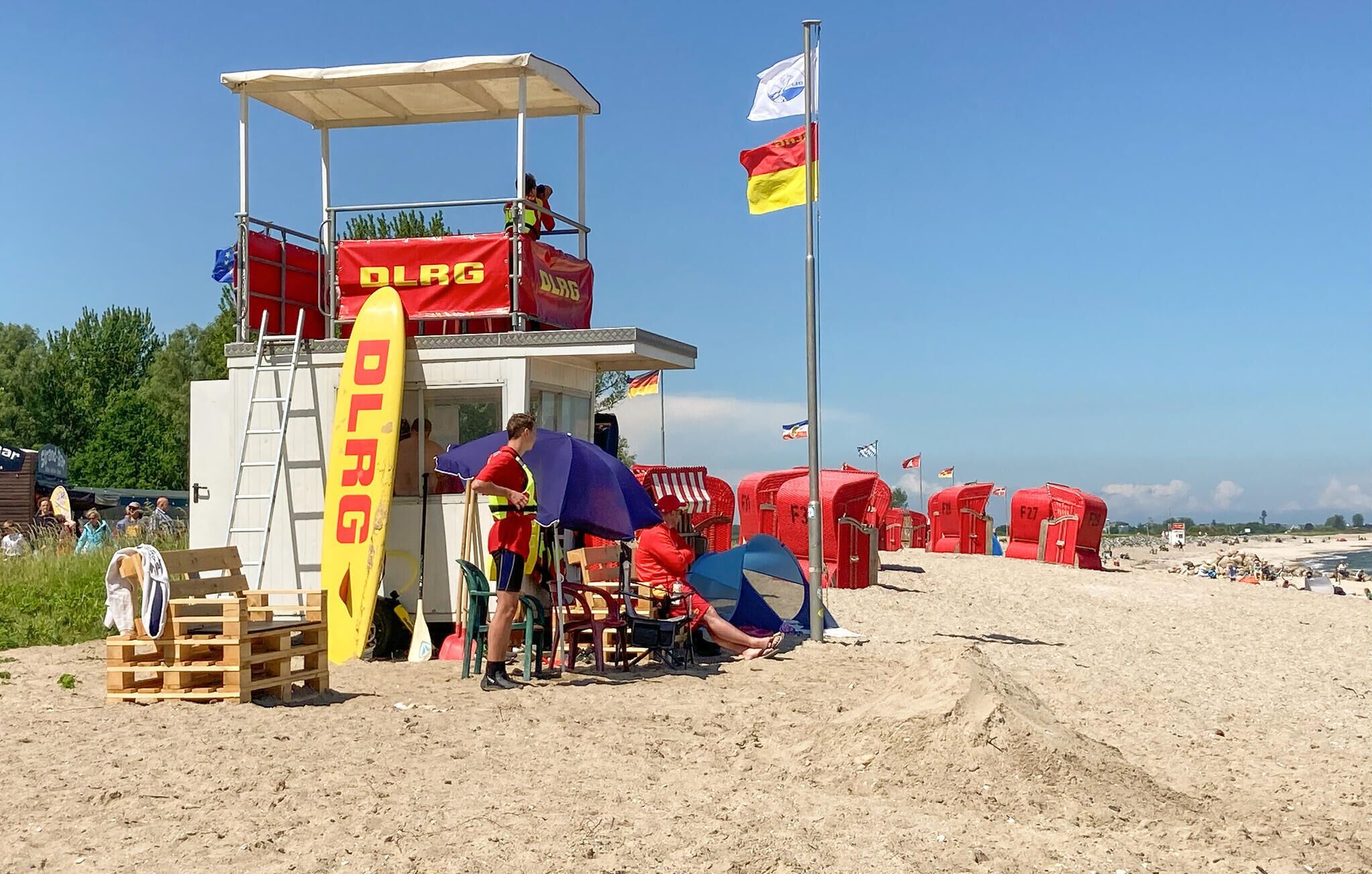 Ein Rettungsschwimmturm mit rotem Banner, einer Flagge und Strandsonnenschirmen.