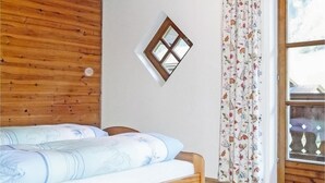 Una camera da letto con soffitto in legno, un letto con biancheria a fantasia, una finestra con cornice decorativa e una tenda con motivo floreale.