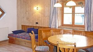 Una stanza accogliente con pavimento in legno, un divano a quadri, un tavolo da pranzo in legno con sedie e una finestra con tende.