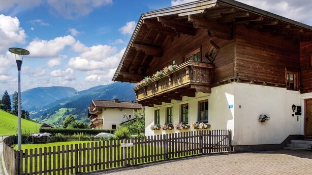 Un chalet tradizionale con facciata in legno, un balcone con cassette di fiori e vista sulle montagne.