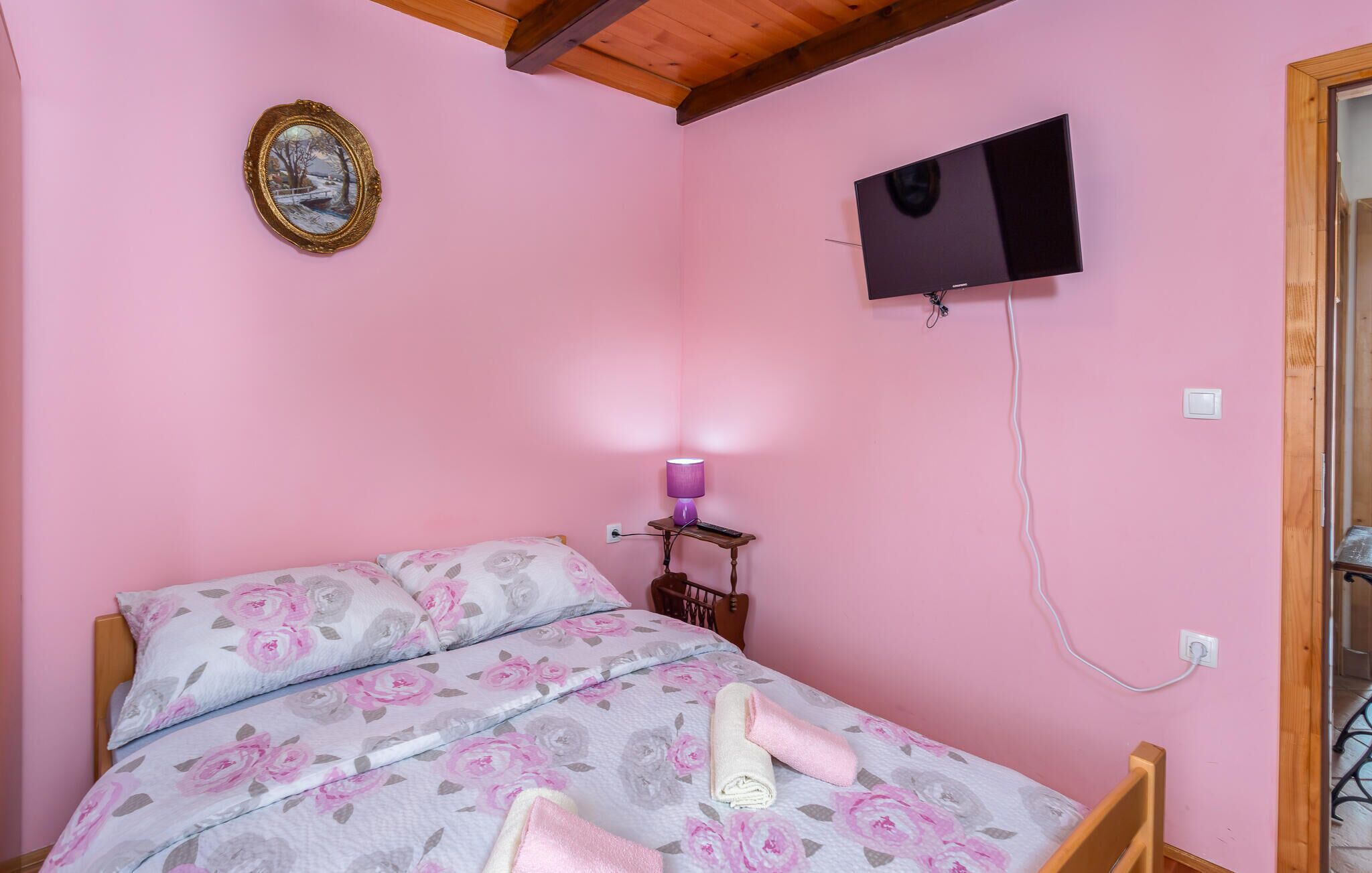 Une chambre à coucher comprenant un lit, un téléviseur fixé au mur, une table de chevet avec une lampe et un cadre photo accroché au mur.