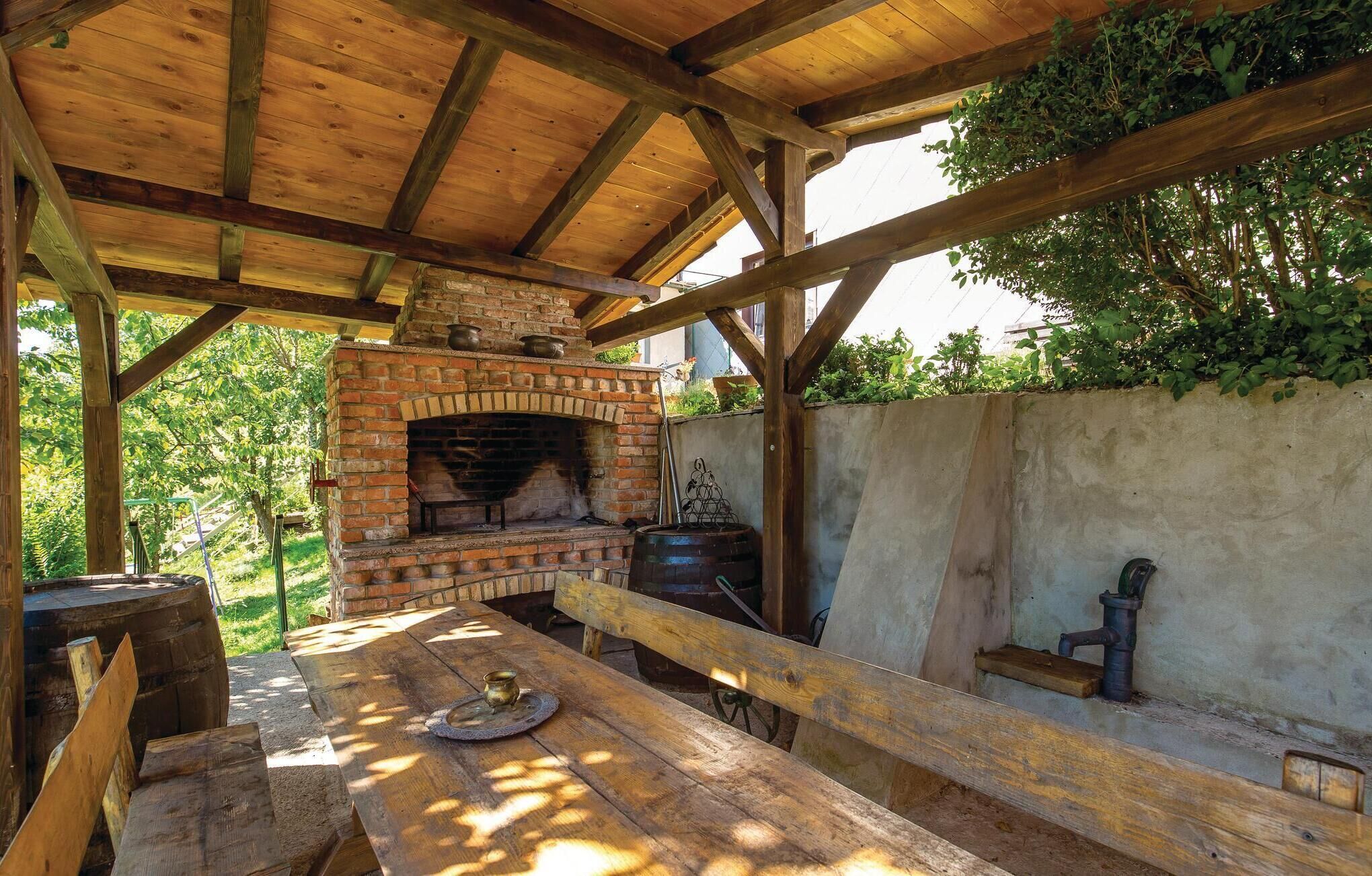 An outdoor brick oven under a wooden roof, a wooden table, and a barrel.