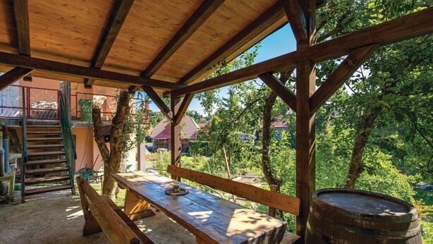 An outdoor wooden structure with a bench and a barrel, surrounded by trees and a view of houses in the background. - 3 bedroom nice home in Fuzine (Fuzine)
