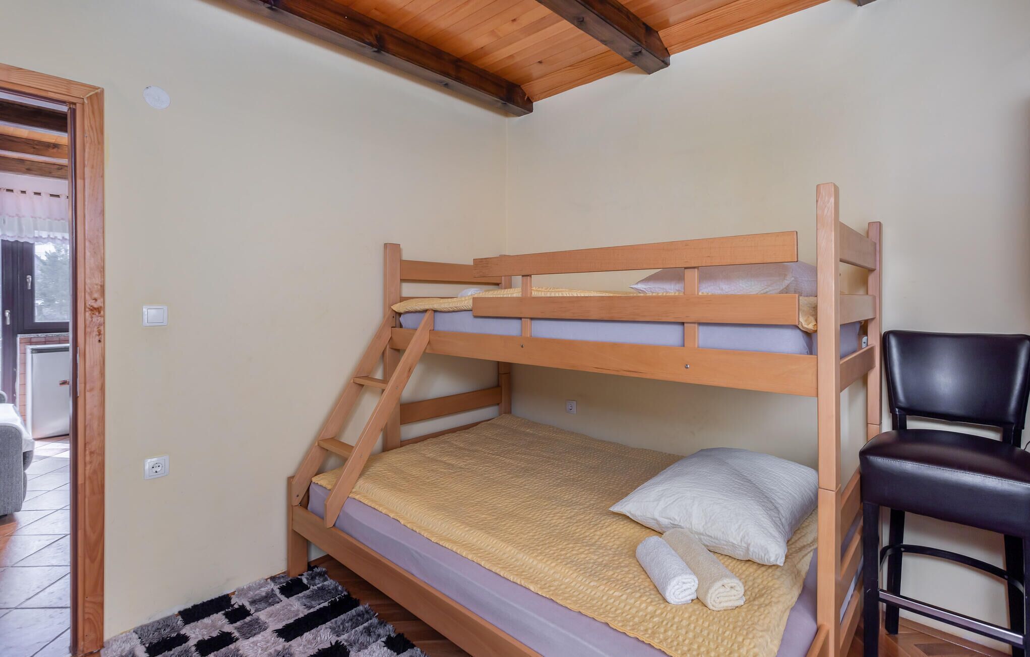 A bunk bed with a wooden frame, a white pillow, and a rolled towel on the lower bunk.