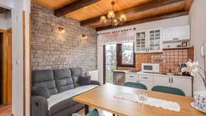 A cozy living room with a sofa, a wooden dining table, and a kitchen area with cabinets and a microwave. - 3 bedroom nice home in Fuzine (Fuzine)