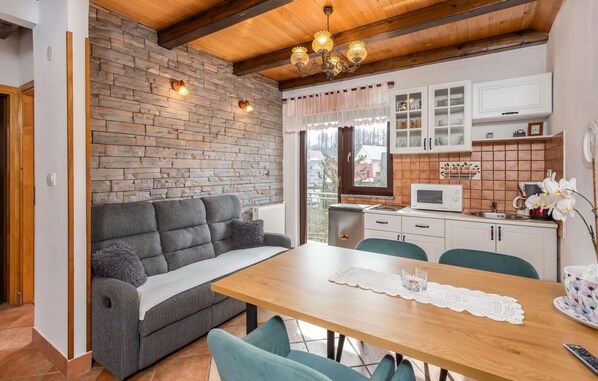 Een gezellige woonkamer met een bank, een houten eettafel en een keuken met kastjes en een magnetron.