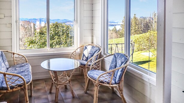 A corner room with a glass table and wicker chairs, large windows with a view of a green landscape and mountains. - Amazing home in Tau with house sea view (Tau)