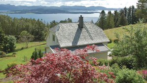 A house with a sloped roof, surrounded by a lush garden and a view of a lake and mountains. - Amazing home in Tau with house sea view (Tau)