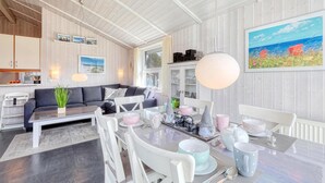 Un salon moderne avec un canapé, une table à manger et des chaises. On y trouve des tableaux encadrés au mur, une grande fenêtre et une peinture.