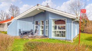 Une maison bleue de plain-pied, dotée d’un patio couvert, d’un coin repas et d’un numéro « 12 » bien visible sur le côté.