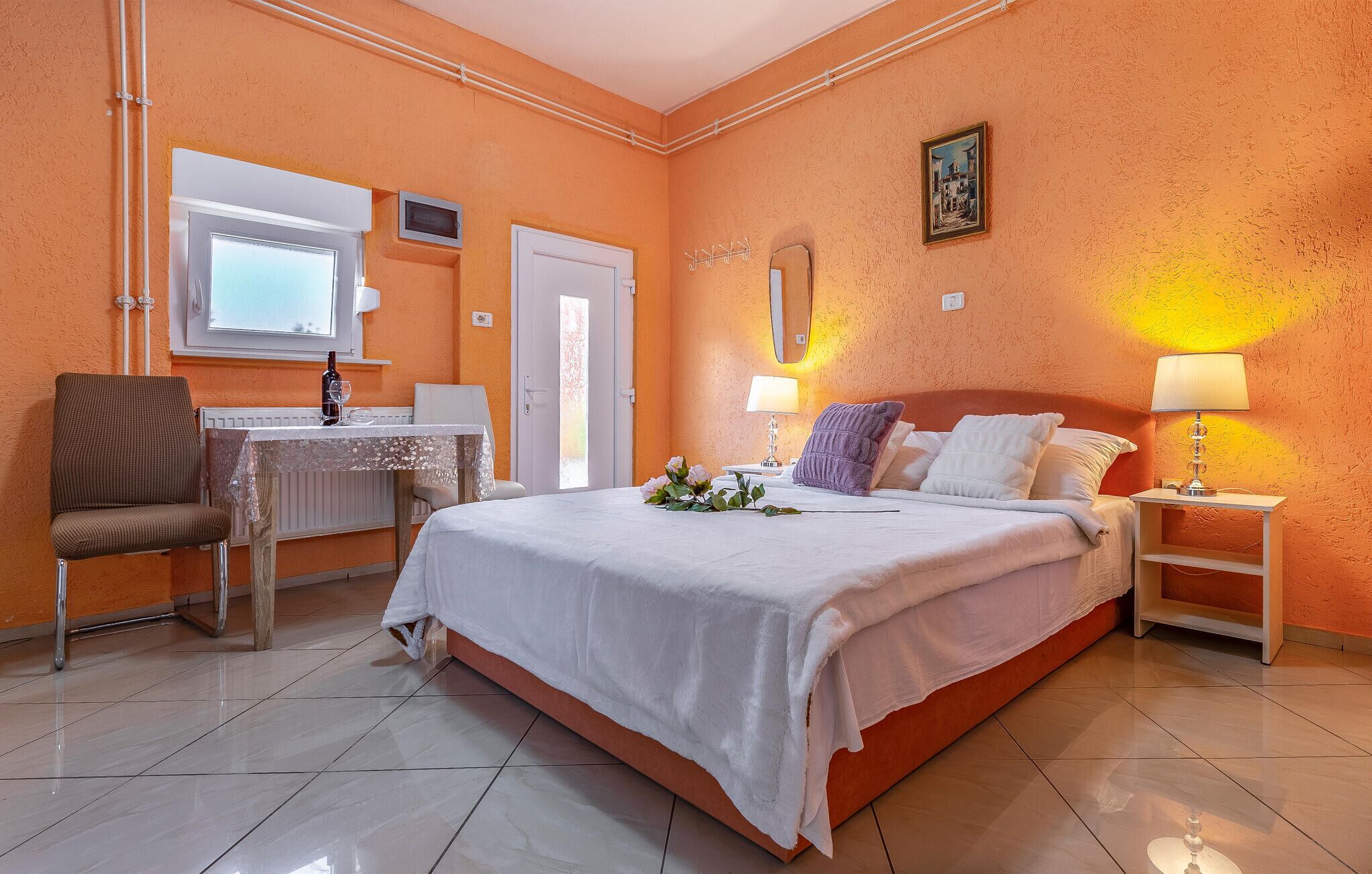 Una habitación de hotel con cama, escritorio, silla, espejo y mesita de noche con lámpara.