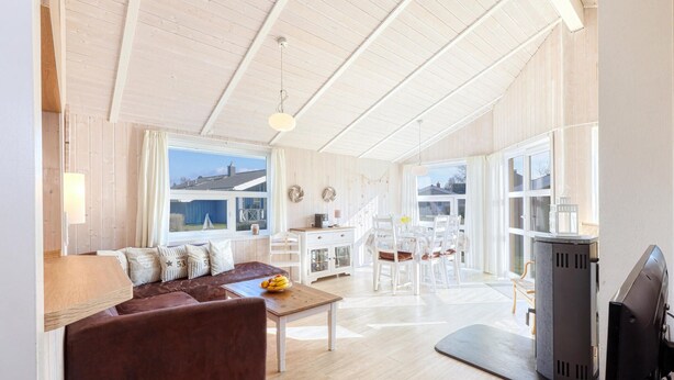 A spacious living area with a brown sofa, a dining table, and a TV. There are large windows and a view of the outside. - Beautiful home in Schönhagen with sauna (Schönhagen)