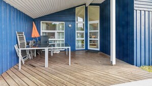 Une terrasse couverte avec une table et des chaises, un mur extérieur bleu et une porte-fenêtre coulissante.