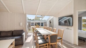 Une pièce spacieuse comprenant une longue table à manger, des chaises en bois, un canapé et un téléviseur fixé au mur.
