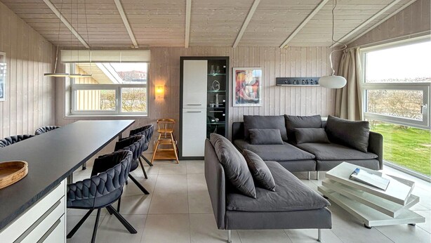 A modern living room with a sofa, dining table, chairs, and a kitchen area.