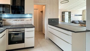 A modern kitchen with a built-in oven, a coffee machine, and a view of the beach through a glass wall.