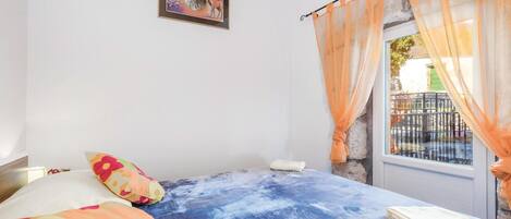A bedroom with a bed, colorful pillows, a framed picture on the wall, and a window with sheer curtains.