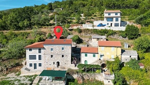 Un edificio de piedra con techo de tejas rojas, rodeado de abundante vegetación y otros edificios.